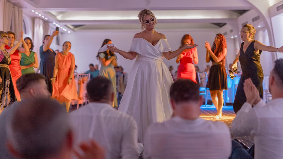 A lively wedding celebration featuring a bride dancing with guests in an elegant indoor setting.